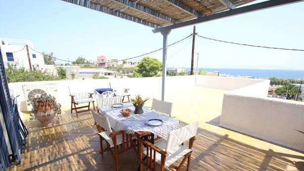 Eine Terrasse im Freien mit einem Tisch für zwei Personen, umgeben von Holzstühlen, mit Blick auf die Küste.