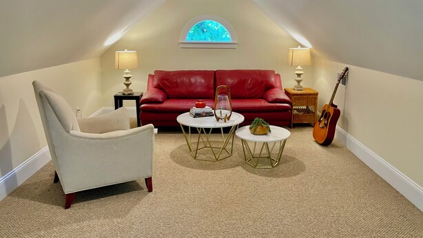 Ein gemütliches Schlafzimmer im Loft-Stil mit einem roten Ledersofa, einem weißen Sessel, einem kleinen runden Tisch und einer Gitarre.