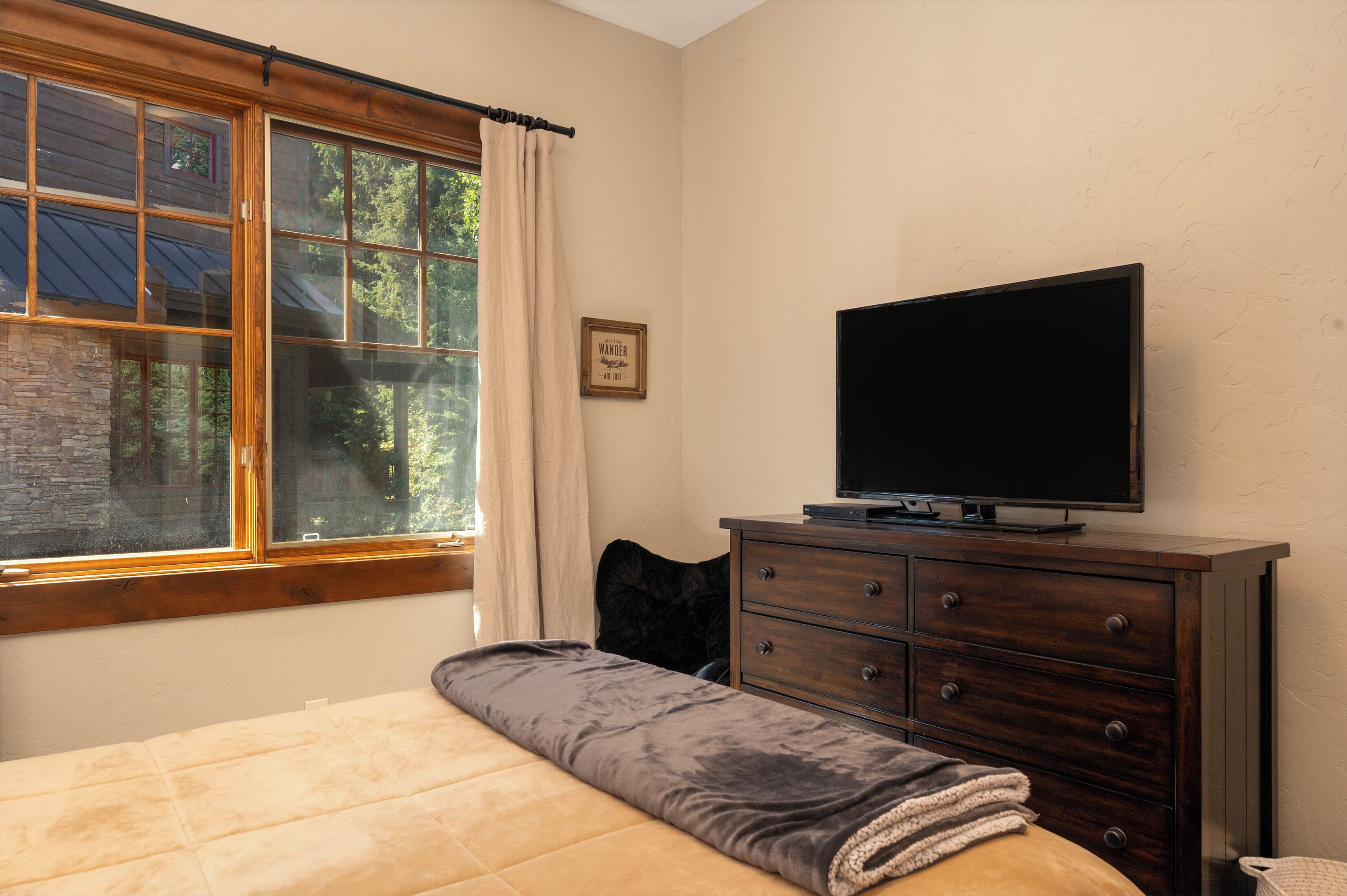 Un dormitorio con una cama, un tocador, un televisor y una ventana con cortinas.
