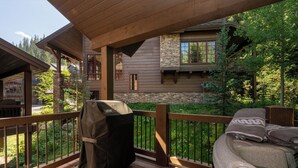 Una terraza de madera con una parrilla, un jacuzzi y un muro de piedra.