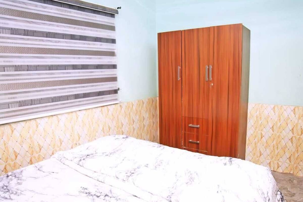 A bedroom with a bed, a wardrobe, and a window with blinds.