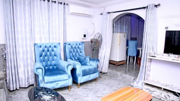 Una sala de estar con un sofá azul, una mesa de centro de madera y un televisor montado en la pared.