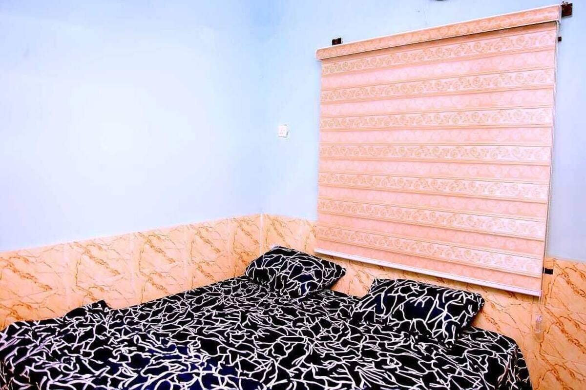 A bedroom with a bed, a patterned headboard, and a window with a blind.