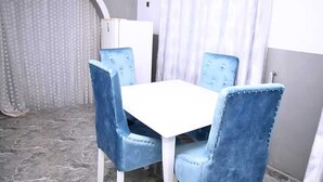 Un comedor con una mesa blanca y sillas tapizadas en azul, un armario blanco y una cortina estampada.