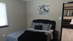 Een slaapkamer met een bed, een zwart hoofdbord, een grijze deken en een schilderij aan de muur.