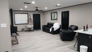 Een moderne woonkamer met een leren zwarte bank, een hangstoel, een eethoek met een marmeren tafel, en een plafondventilator.