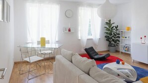 Un salon moderne avec une table à manger en verre, un canapé, un fauteuil noir, un tapis rouge et une plante en pot.