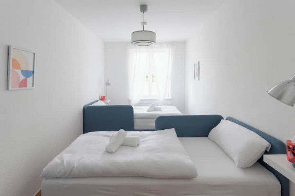 Ein modernes Hotelzimmer mit einem ordentlich bezogenen Bett, einem großen Fenster mit durchsichtigen Vorhängen und einer minimalistischen Einrichtung.
