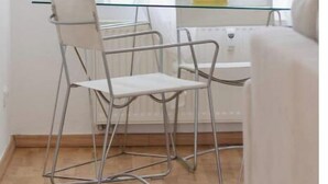 Un coin repas avec une table en verre et des chaises en métal, un radiateur et une fenêtre ornée de rideaux légers.
