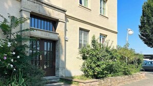 Un bâtiment doté d’une façade en pierre, d’une porte en bois sombre et d’un petit jardin agrémenté de plantes et de fleurs.