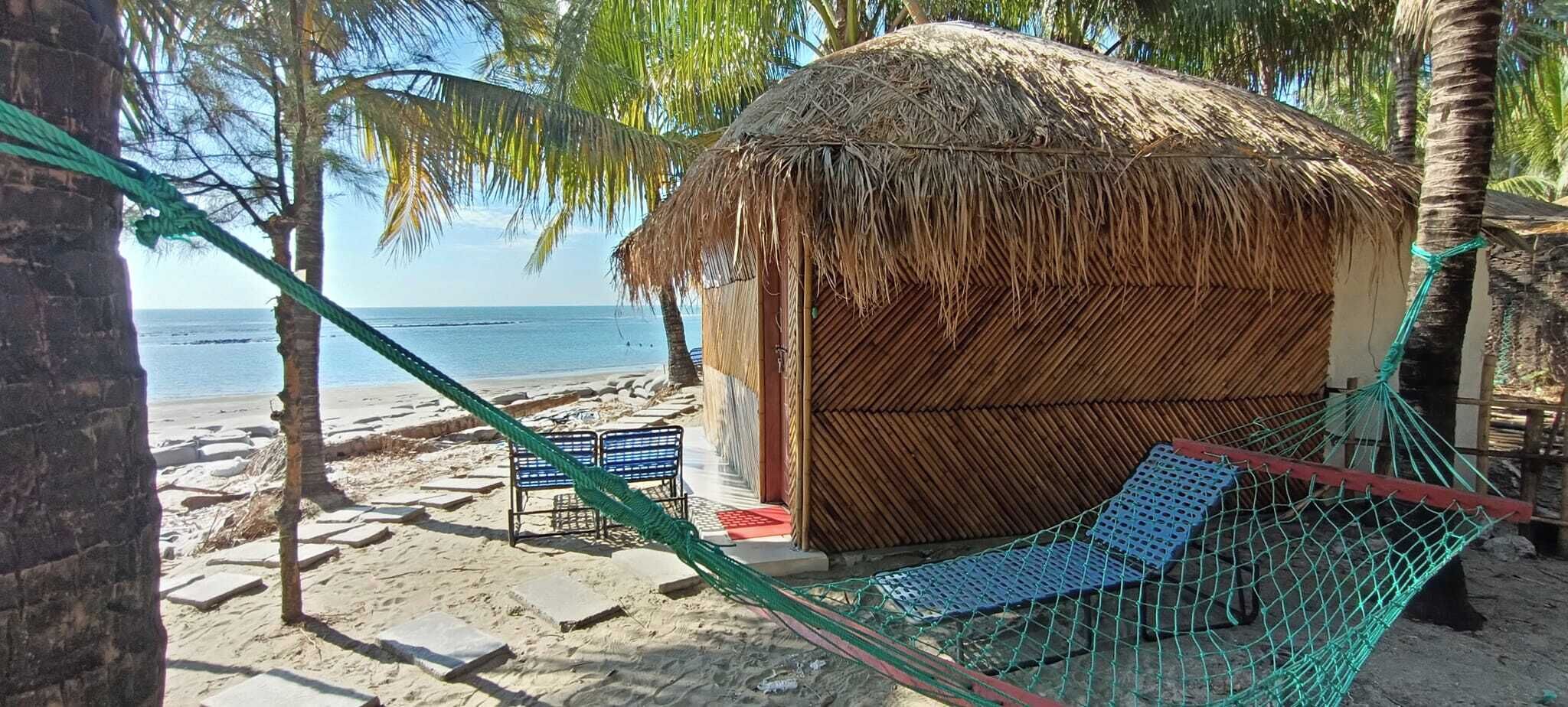 Eine Strandhütte mit einem Reetdach, einer Hängematte und einer Bank.