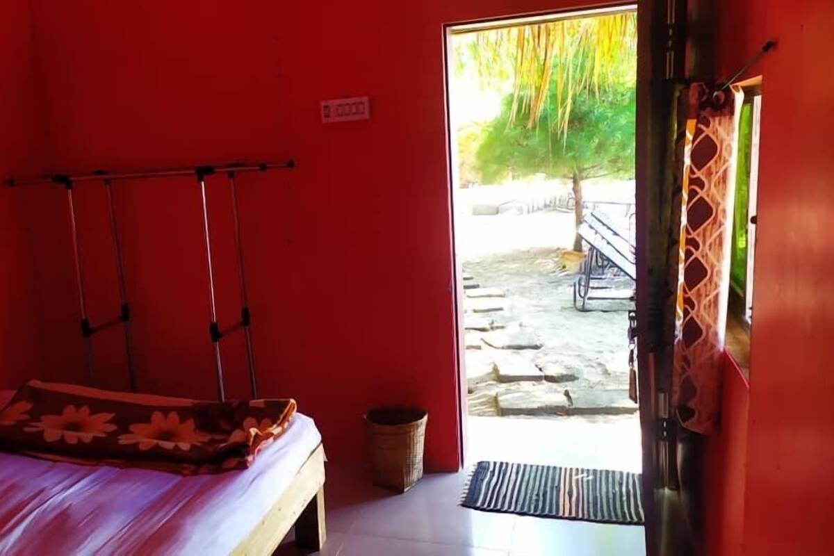 A small room with red walls, a bed with a floral bedspread, a wooden bench, and a wicker basket.