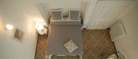 A bedroom with a bed, two bedside tables, a wall-mounted light, a radiator, and patterned flooring.