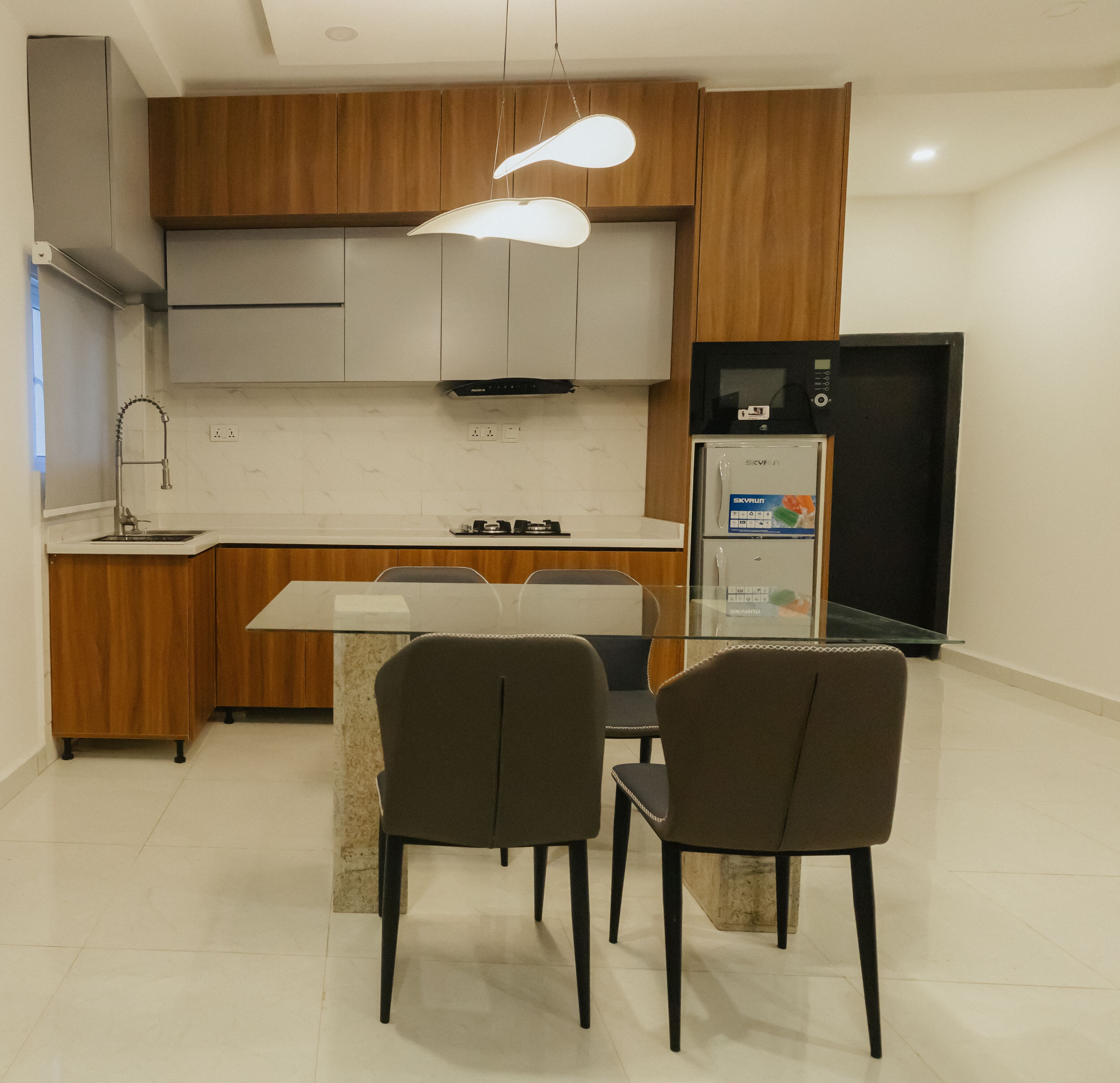 A modern kitchen with wooden cabinets, a built-in microwave, and a refrigerator. There is a dining table with chairs in the center.