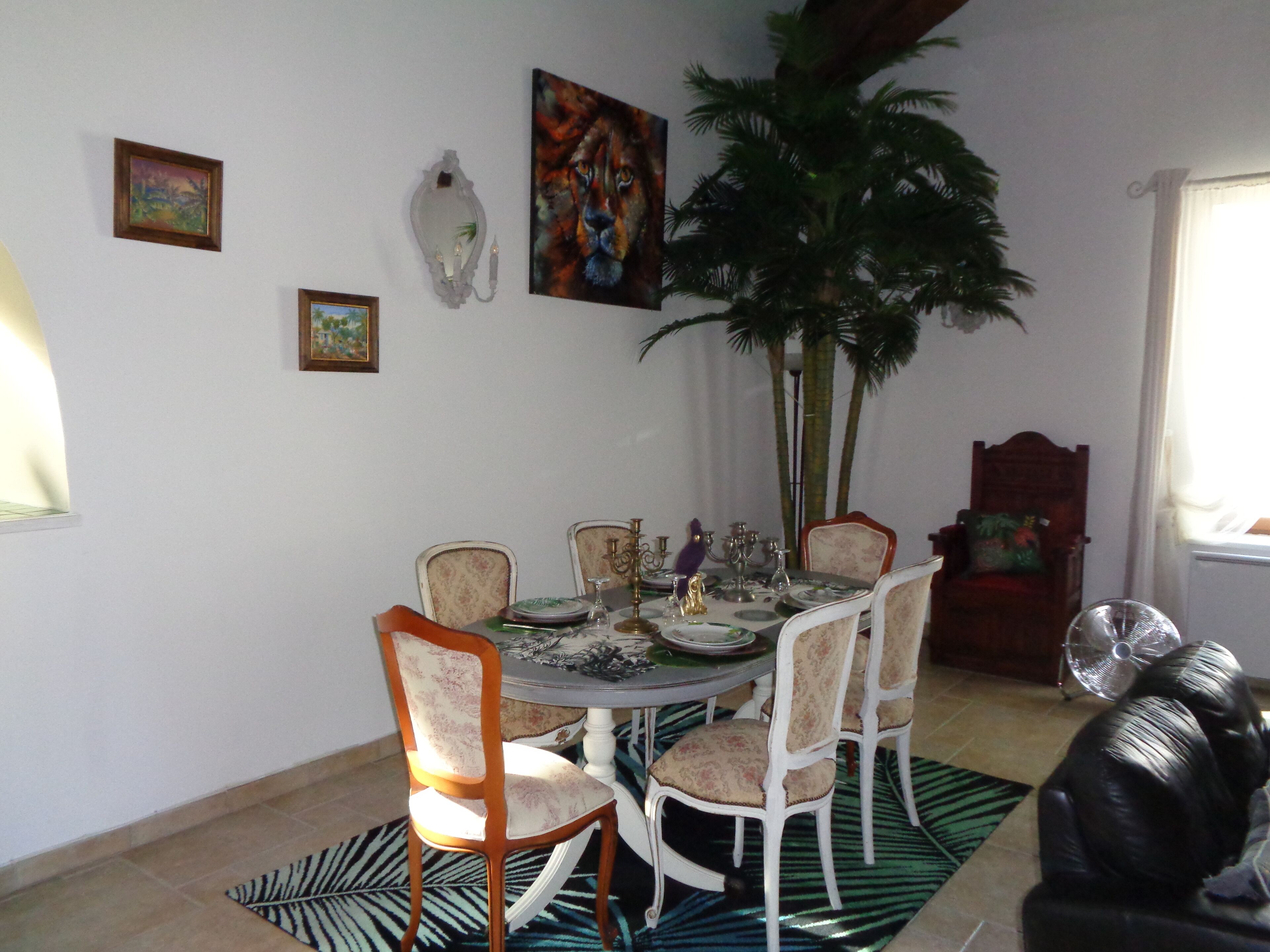Een eetgedeelte met een ronde tafel, zes stoelen en een grote potplant.