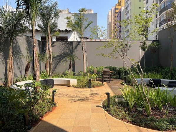 A courtyard with a paved walkway, seating areas, and greenery. - Green Load Saúde (São Paulo)
