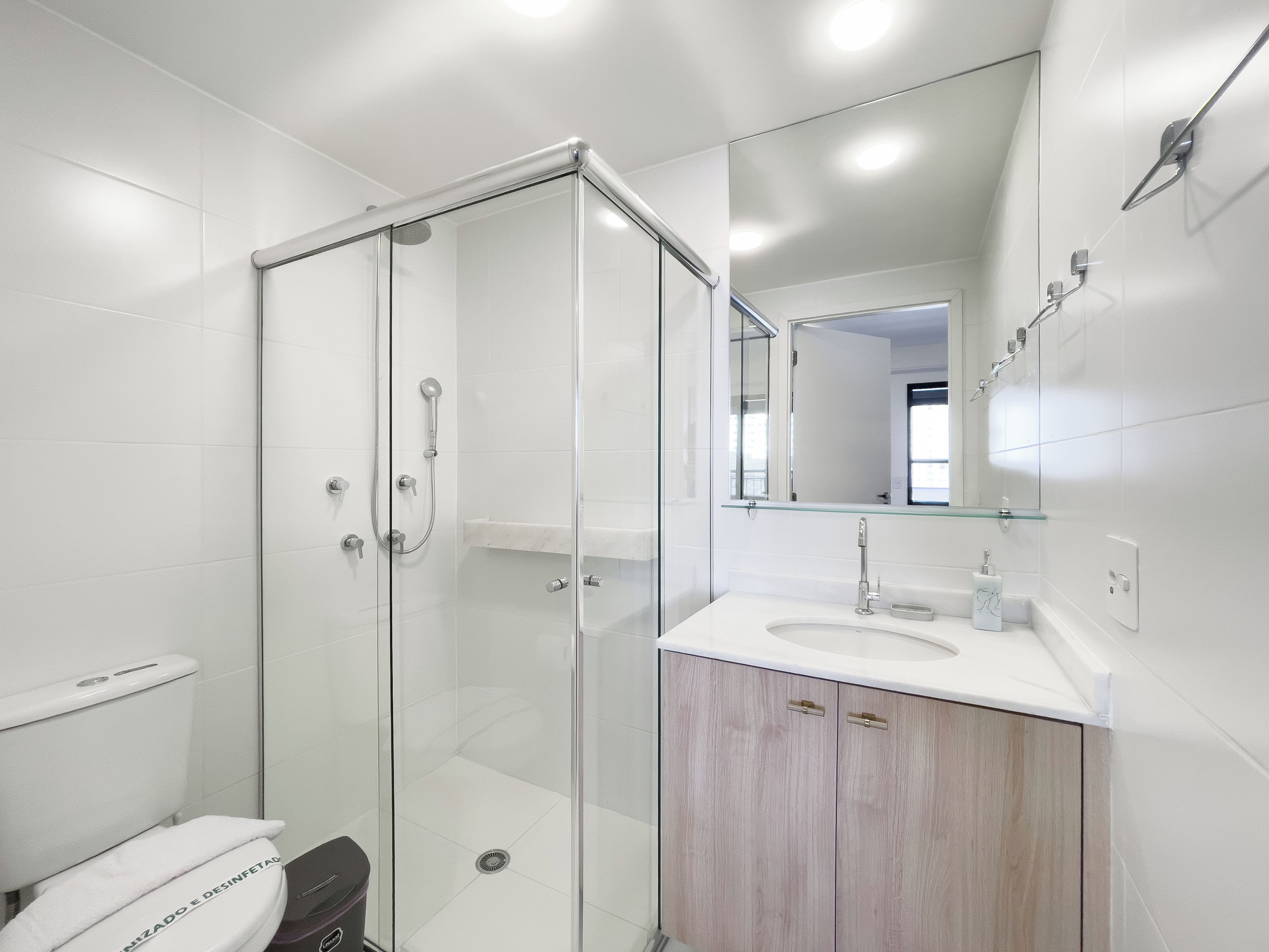 Un baño moderno con ducha envuelta en vidrio, un lavamanos blanco y un mueble de tocador con armarios de madera.