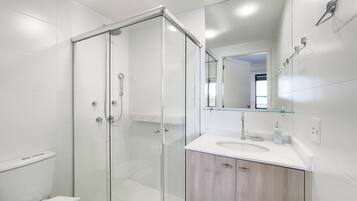 Un baño moderno con ducha envuelta en vidrio, un lavamanos blanco y un mueble de tocador con armarios de madera.