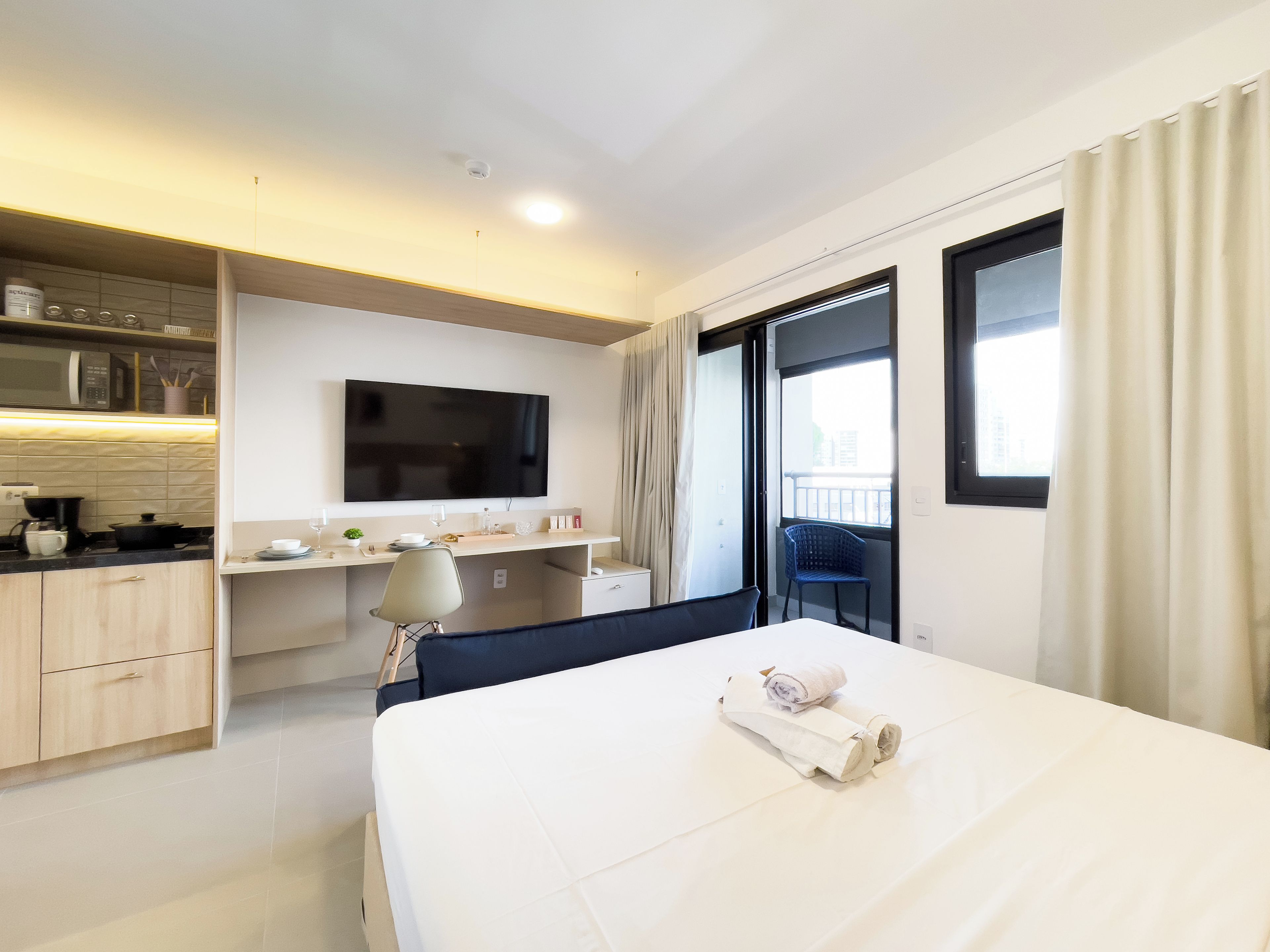 Habitación de hotel con cama, escritorio, televisión y balcón.