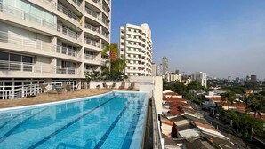 A rooftop swimming pool with a view of surrounding buildings and a clear sky.