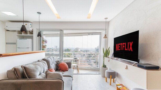 A modern living room with a sofa, a TV mounted on the wall, and a balcony with a city view.
