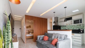 A modern living room with a grey sofa, wooden panel wall, and a kitchen area with a microwave.