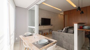 A modern kitchen with a flat-screen TV, a dining area with a table and chairs, and a gray sofa.