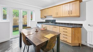 A modern kitchen with wooden cabinets, a granite countertop, and a dining area with a table and chairs. - Cozy Maisonette in Langley Vale  (Epsom)