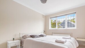A bedroom with a bed, bedside table, and a window with a view of a house and trees. - Cozy Maisonette in Langley Vale  (Epsom)