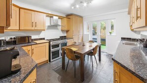 A modern kitchen with wooden cabinets, a granite countertop, a gas stove, and a dining area with chairs. - Cozy Maisonette in Langley Vale  (Epsom)