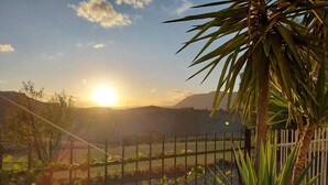 A sunset view over a hilly landscape, with a fence and vegetation in the foreground.