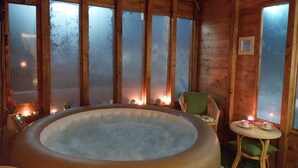 A wooden cabin with a hot tub, large windows, and a small table with cups.