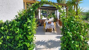 An outdoor patio area with a pergola, a table with chairs, and lush greenery.