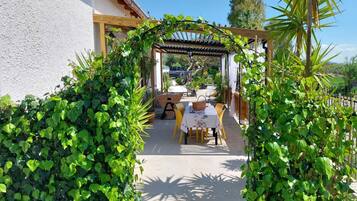 An outdoor patio area with a pergola, a table with chairs, and lush greenery.