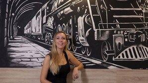A person sitting on a wooden bench with a black and white mural of a train in the background. - Hostel Dos Estaciones (Alicante)