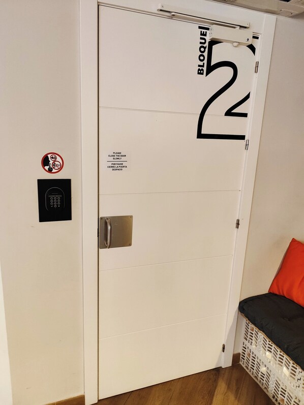 A white door with a security keypad and a sign instructing to close the door slowly. - Hostel Dos Estaciones (Alicante)