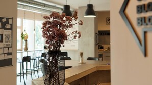 A reception desk with a vase of flowers, a laptop, and a smartphone on it. There is a wall with a sign and a bulletin board in the background. - Hostel Dos Estaciones (Alicante)