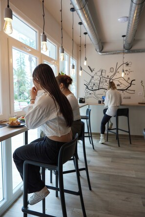 A cafe with high ceilings, exposed ductwork, and hanging light fixtures. - Hostel Dos Estaciones (Alicante)