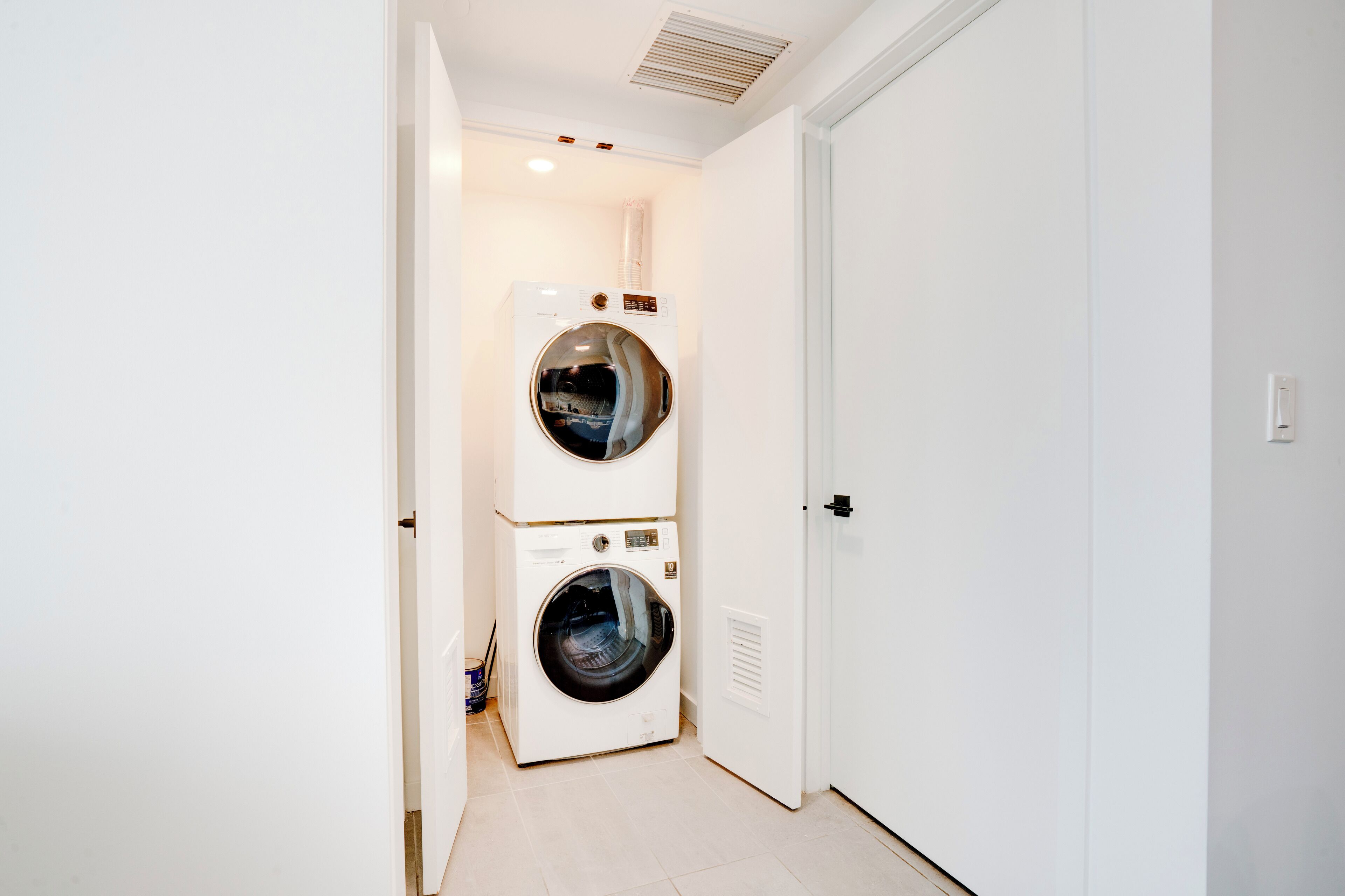A laundry room with two stacked washers and dryers, a door, and a vent on the ceiling.