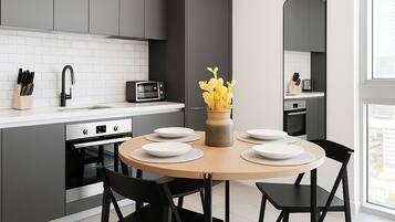 Une cuisine moderne avec des meubles gris, un plan de travail blanc, une table ronde en bois accompagnée de quatre chaises, et un vase rempli de fleurs jaunes.