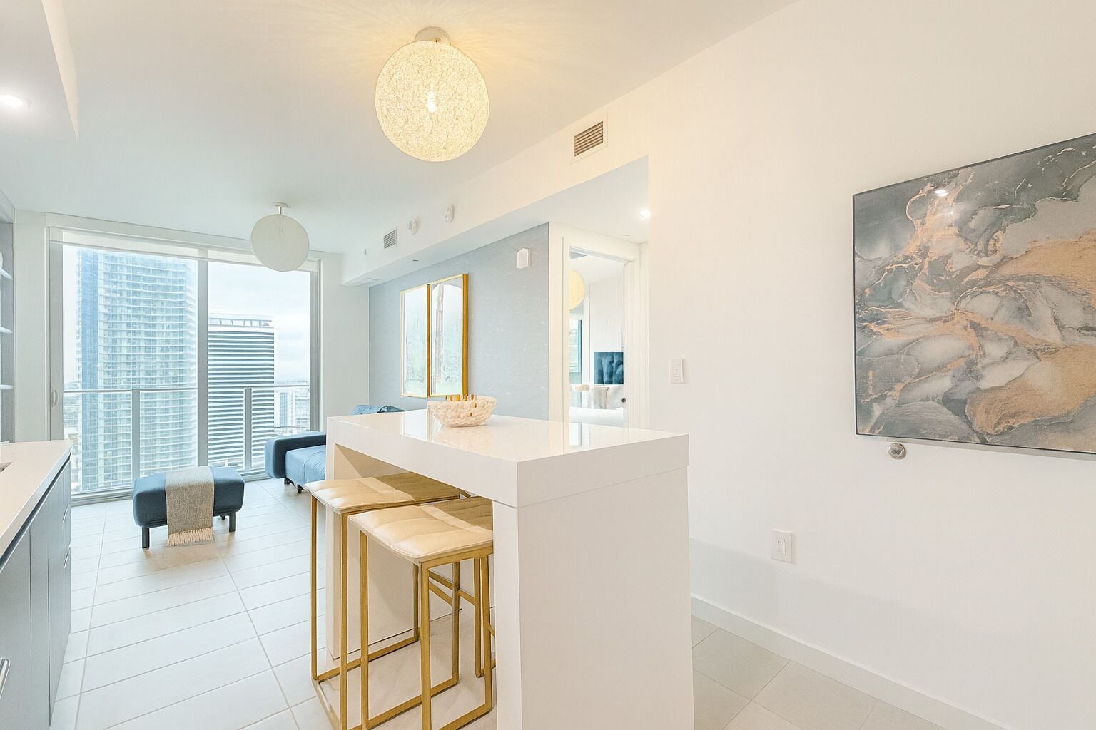 A modern kitchen with a white countertop, bar stools, and a large window.