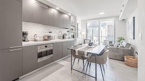 Eine moderne Küche mit grauen Schränken, weißen Arbeitsplatten und einem Essbereich mit Tisch und Stühlen.
