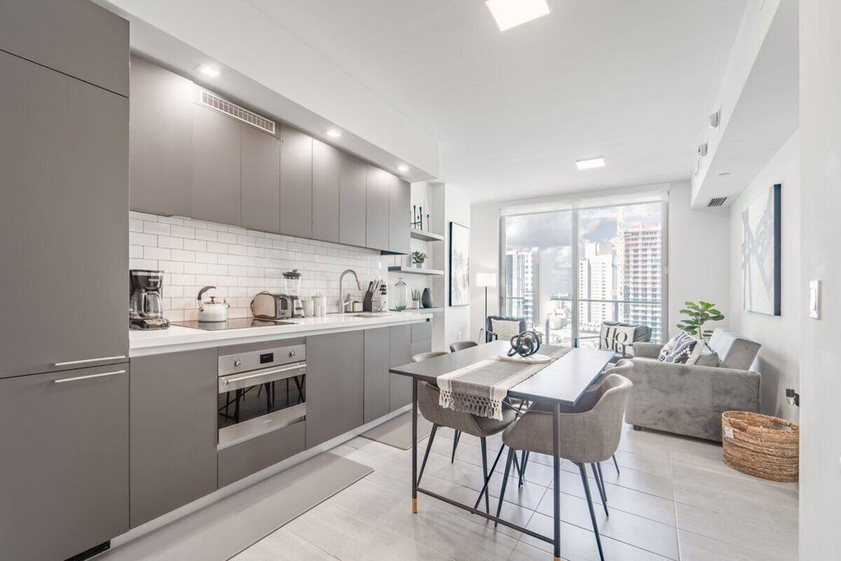 A modern kitchen with grey cabinets, white countertops, and a dining area with a table and chairs.