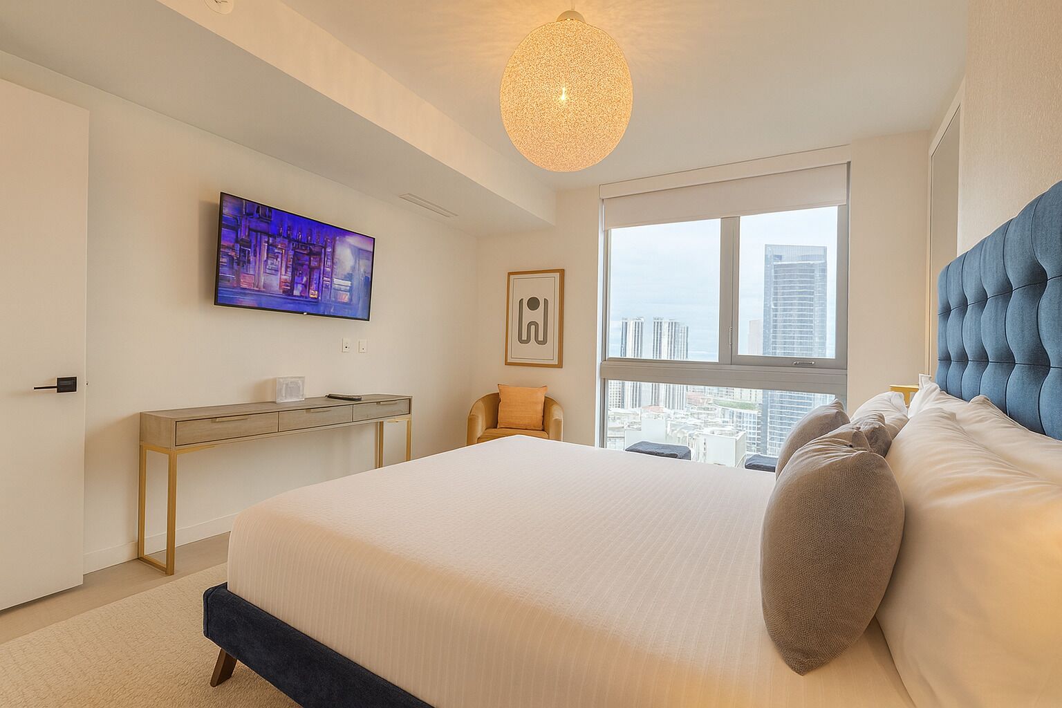 Une chambre d’hôtel moderne, dotée d’un grand lit, d’un bureau, d’une télévision et offrant une vue sur la ville grâce à une grande fenêtre.