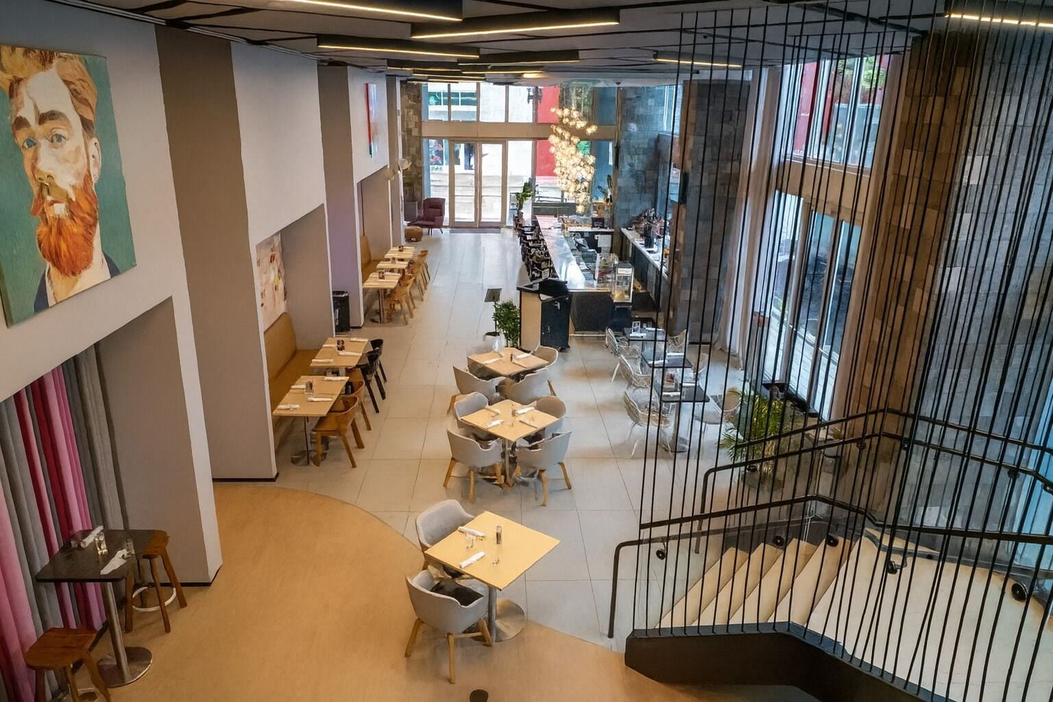 A modern dining area with multiple tables and chairs, a staircase, and a view of the street outside.