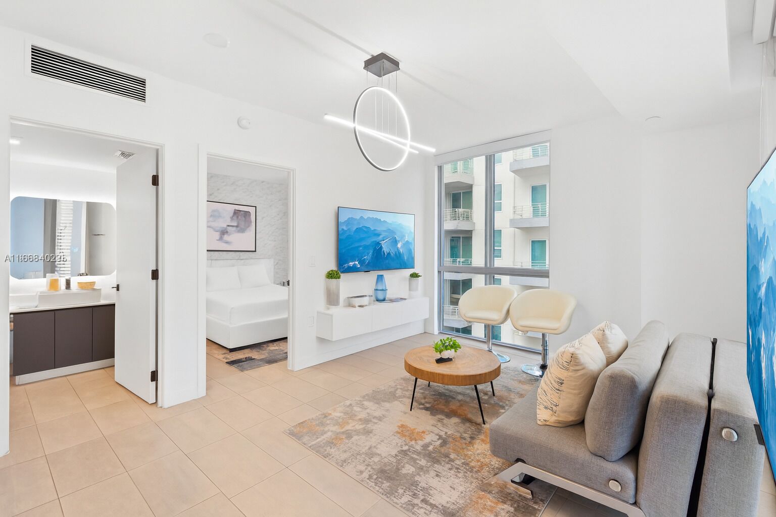 A modern living room with a sofa, a coffee table, and a TV. There is a bathroom with a shower, a sink, and a mirror. The room has large windows and a view of the outside.