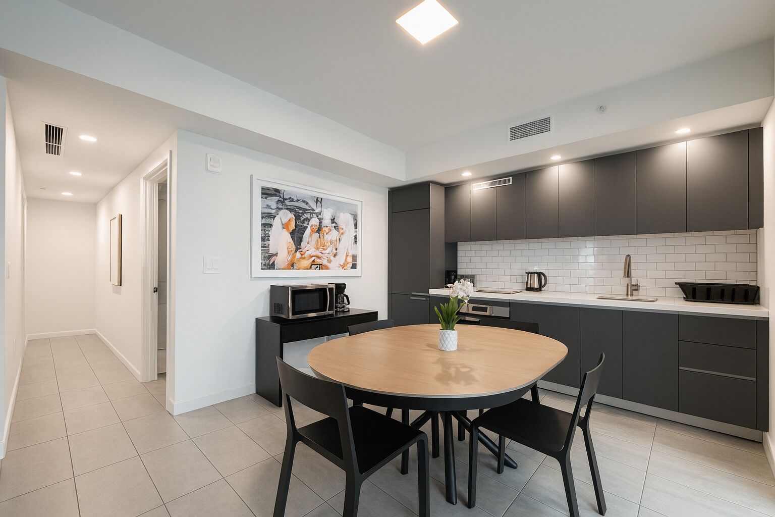 A modern kitchen with dark cabinets, a white countertop, and a round wooden table with chairs.