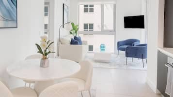 A modern living room with a white sofa, blue armchairs, a round table with chairs, a coffee table, and a TV mounted on the wall.