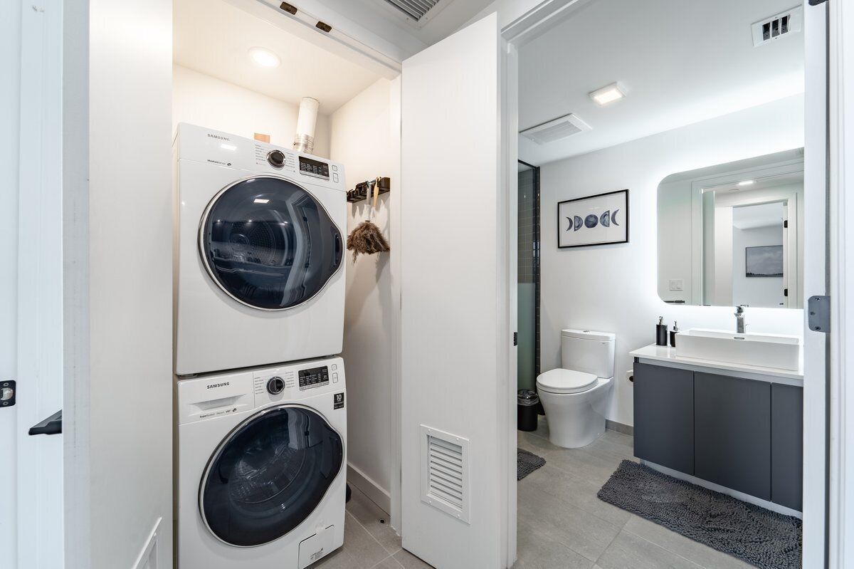 A modern laundry room with stacked washers and dryers, a toilet, and a vanity with a mirror.