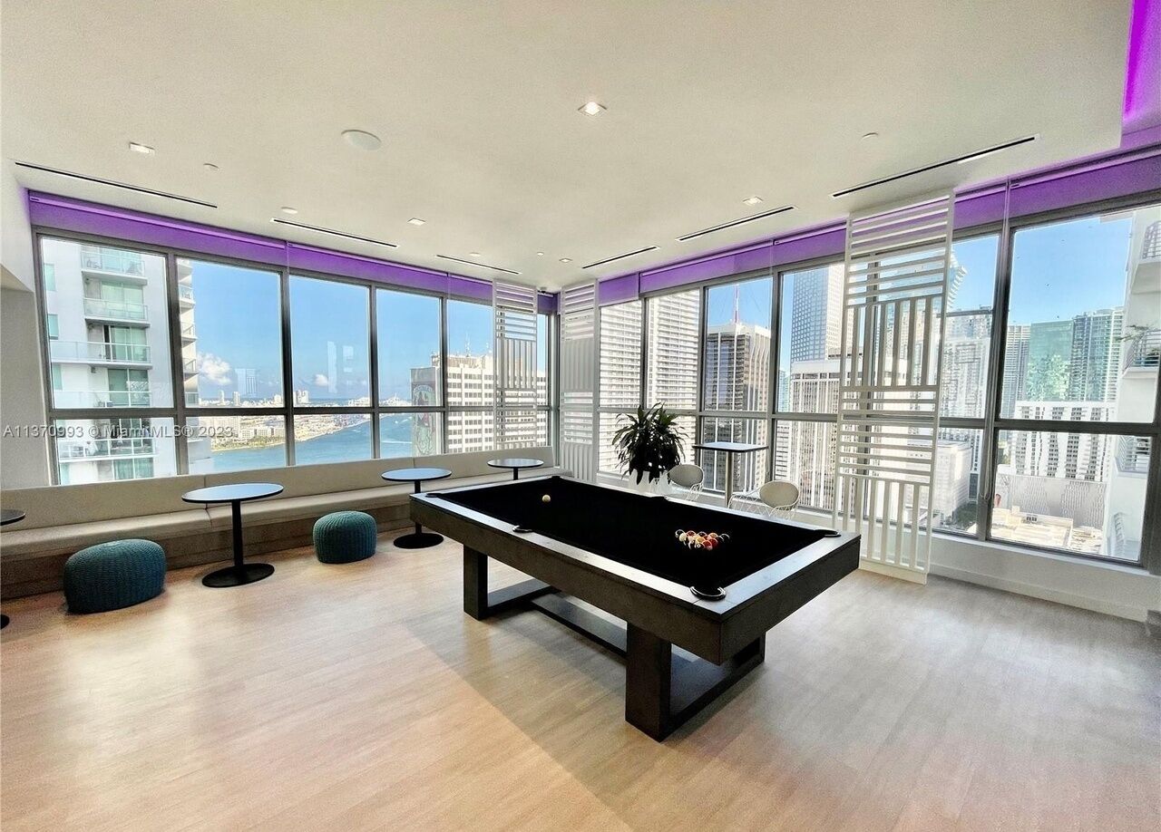 Une table de billard dans une pièce moderne dotée de grandes fenêtres donnant sur la ville.